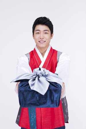 Young Asian man in Hanbok, Korean traditional clothes, posing with a gift - isolated on whiteの写真素材