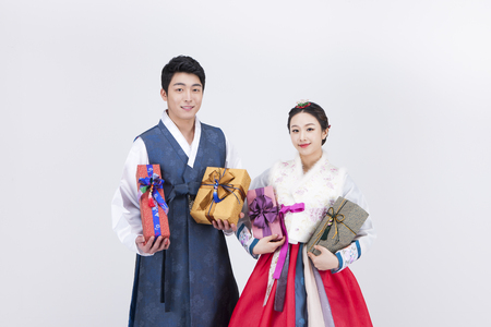 Young Asian couple in Hanbok, Korean traditional clothes, posing with gift boxes - isolated on whiteの写真素材