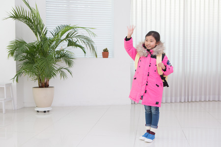 Little Asian girl in heavy winter jacket and mittens waving her handの写真素材