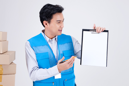 Asian delivery man wearing uniform isolated in white - standing with boxes of shipmentsの写真素材