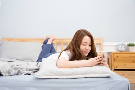 Young female Asian using a smart phone/cellular phone lying in bedのeditorial素材