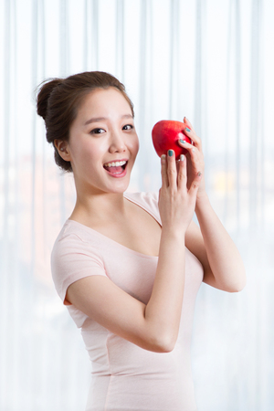 Young female Asian holding a fresh fruit in white interior roomの写真素材