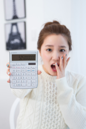 Young female Asian showing a calculator to the front with surprised faceの写真素材