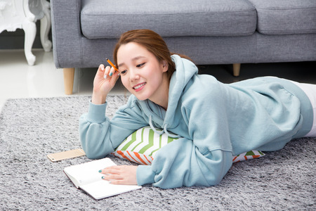 Young female Asian reading books on living room floor