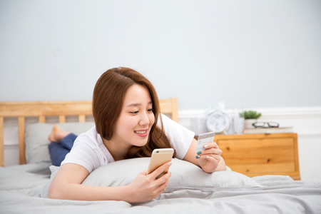 Young female Asian using a smart phone/cellular phone lying in bedのeditorial素材