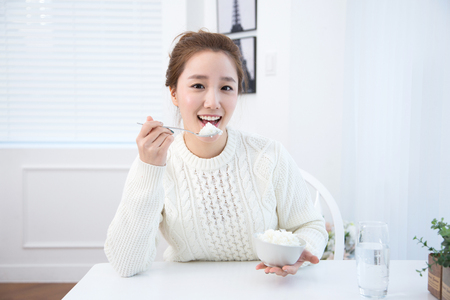 Young female Asian eating a bowl of rice in white interior roomの写真素材