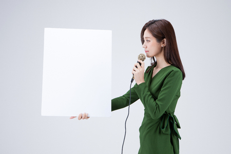 Isolated shot in studio - Asian career woman in green dress posing with white empty boardの写真素材