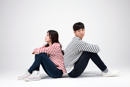 Isolated shot in studio - Asian young couple wearing matching shirts sitting down on the floorの写真素材