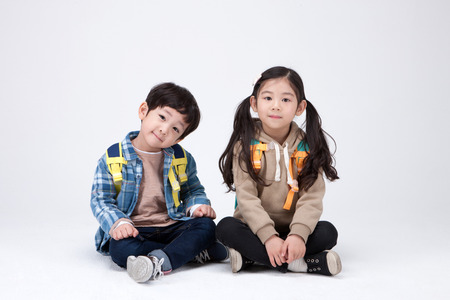 Isolated shot in studio - little Asian girl and boy posing together as sitting down with legs crossedの写真素材