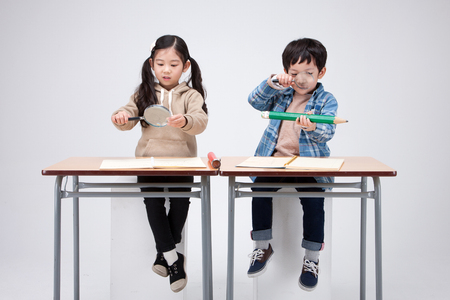 Isolated shot in studio - little Asian girl and boy sitting at desk and posing togetherの写真素材