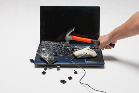 Damaged/Smashed/Broken laptop with a hand holding a hammer isolated in white background