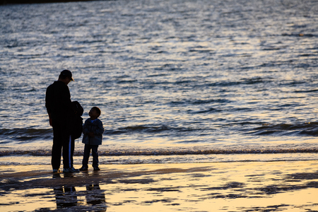 Back shot of children playing with father on the beach at sunsetの写真素材