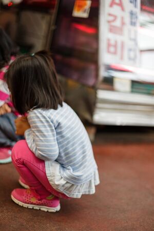 Korean traditional market - a little girl watching curiously while squatting downの写真素材
