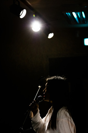 An Asian female singing on the lit stage as holding micのeditorial素材