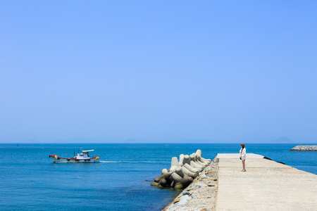 Slow city island-A woman standing on waterbreaks in windの写真素材