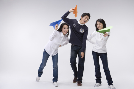 Two Asian women and a man posing together in a studio with paper airplaneの写真素材