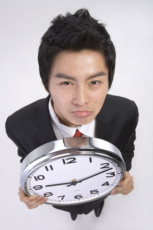 Asian man in suit posing in a studio with a round wall clockの写真素材