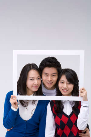 Two Asian women and a man posing together in a studio with photoframe