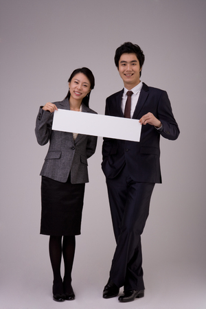 Asian woman and a man in suits posing in a studio holding an empty white paper/boardの写真素材