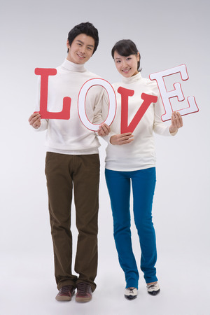 A couple of young Asian man and woman posing in a studio with LOVE letter propsの写真素材