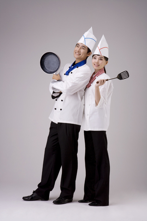 Male and female chef/cook posing in a studio together with cooker/cooking utensilsの写真素材