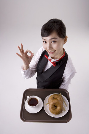 Asian female waitress posing in a studio with a tray of bagels and coffeeの写真素材