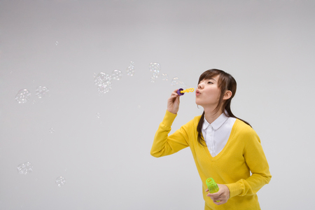 Asian girl posing in a studio making soap bubblesの写真素材