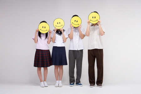 Four Asian teenagers in school uniforms posing in a studio with smiley emoticon face propsの写真素材