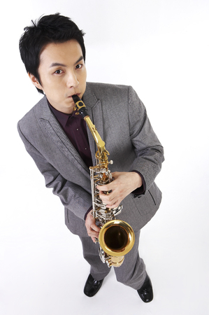 Dressed up Asian male posing in a studio with saxophoneの写真素材