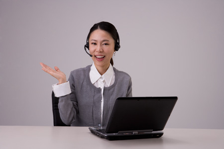 Female telemarketer posing in a studio as sitting at desk with laptop/computerの写真素材