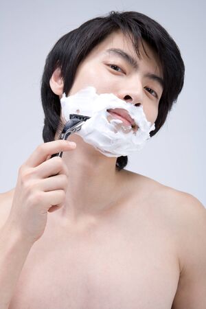 Asian boy shaving chin with razor in a studioの写真素材