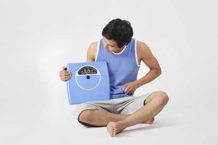Young Asian male in training suits posing in a studio with weight scaleの写真素材