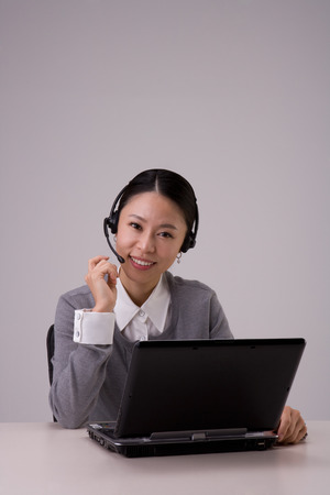 Female telemarketer posing in a studio as sitting at desk with laptop/computerのeditorial素材