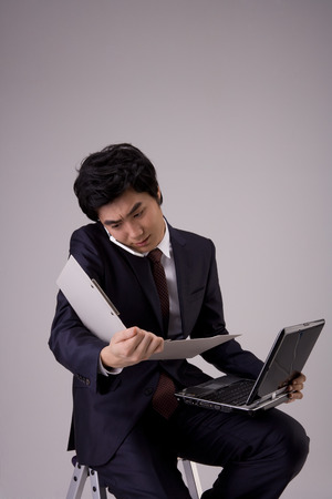 Asian man in suit posing in a studio with laptopの写真素材