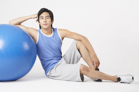 Young Asian male in training suit posing in a studio with gym ballの写真素材