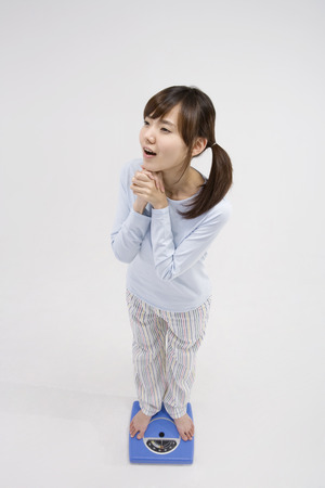 Young Asian female wearing pajamas posing in a studio with weight scaleの写真素材