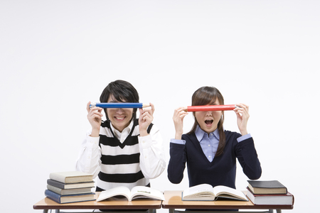 Asian male and female students posing in a studio as sitting at desk with books and pencilの写真素材