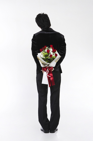 Male Asian in suit posing in a studio with a bouquet of flowers/red rosesの写真素材