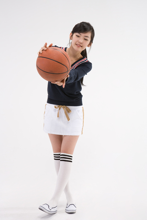 Asian girl teenager in school gym unifrom posing in a studio with basketballの写真素材