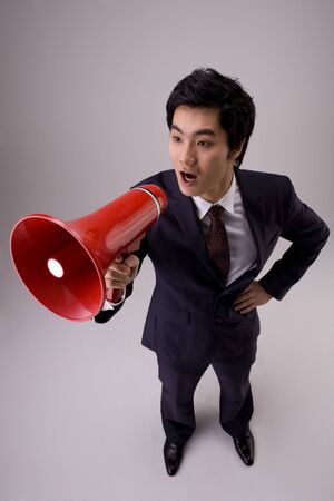 Asian man in suit posing in a studio with megaphoneの写真素材