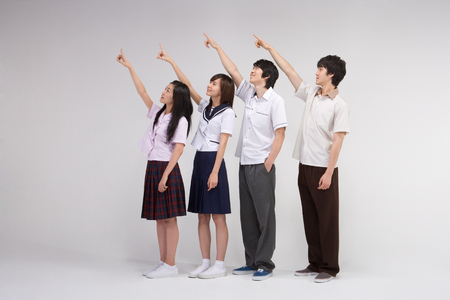 Four Asian teenagers in school uniforms posing in a studio with hand gesturesの写真素材