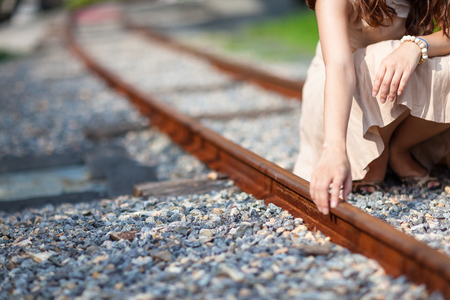 A woman touching the rusty train rail as sitting down in the middle of train tracksの写真素材