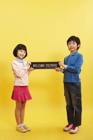 Young Asian boy and girl posing in a studio with welcome friends signの写真素材