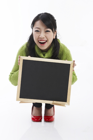 Young female Asian posing in a studio with empty black boardの写真素材