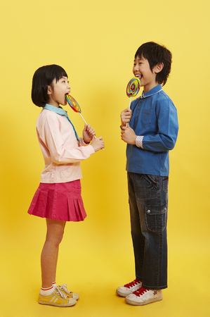 Young Asian boy and girl posing in a studio with lollipopsの写真素材