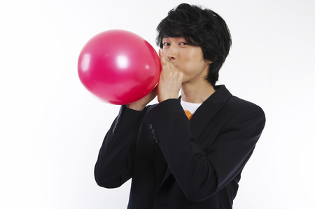Young male Asian in black jacket posing in a studio with balloonの写真素材