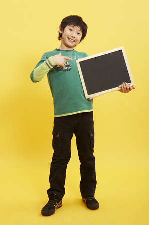 Young Asian boy posing in a studio with empty black boardの写真素材