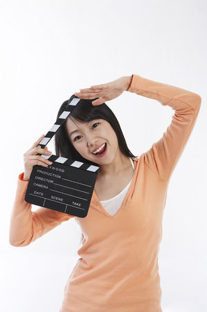Young female Asian in orange shirt posing in a studio with movie director clapper boardの写真素材