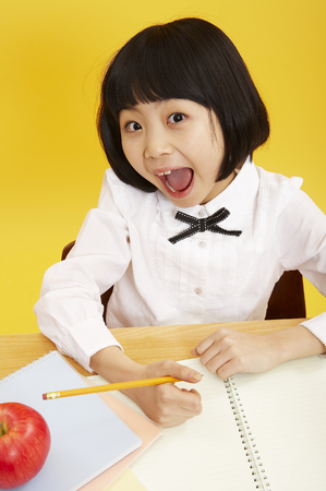Young Asian girl in school uniform posing in a studio studying at deskの写真素材