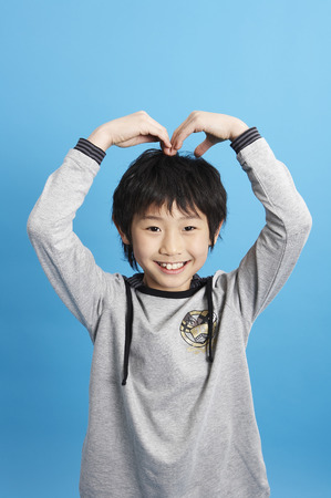 Young Aisn boy posing in a studio as making a heart with armsの写真素材